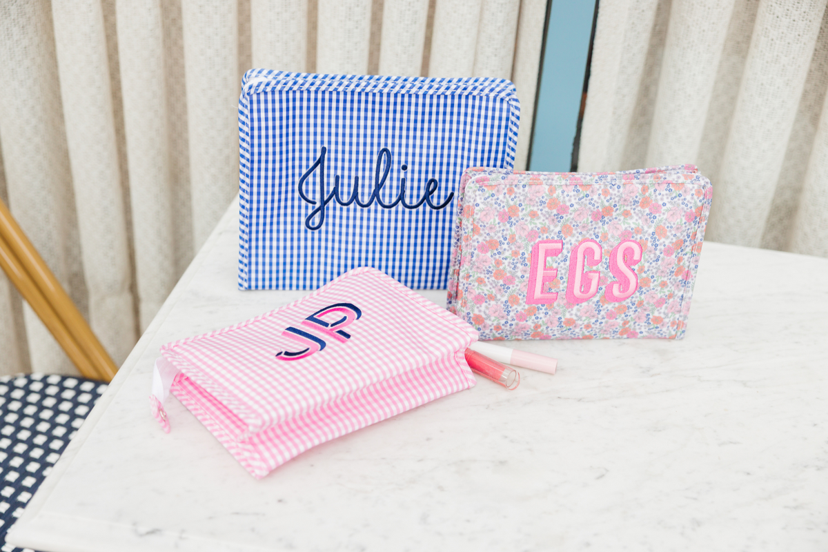 Three personalized pouches: a blue gingham pouch, a floral pouch and a pink striped pouch.