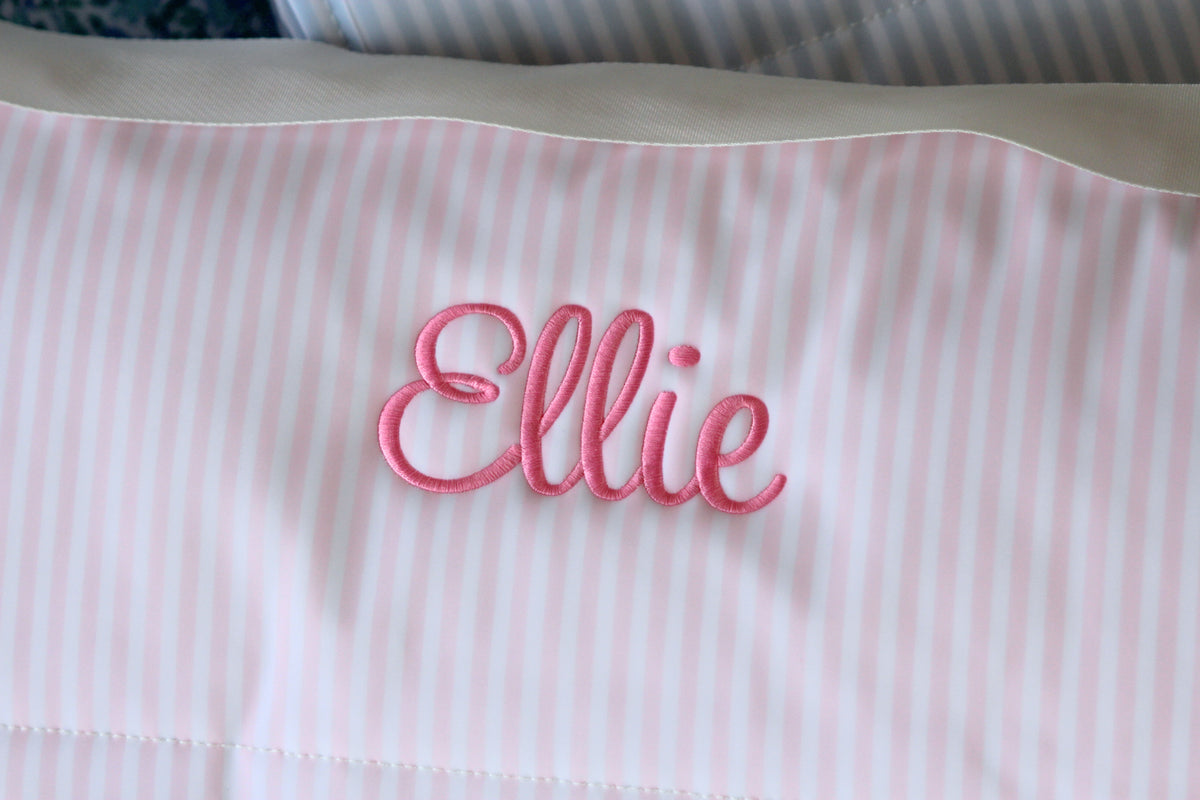 Close-up view of a pink striped Nap Mat with white trim, featuring the name "Ellie" beautifully embroidered in bright pink thread. The cozy and personalized design is ideal for preschool naps, daycare rest time, or travel comfort.