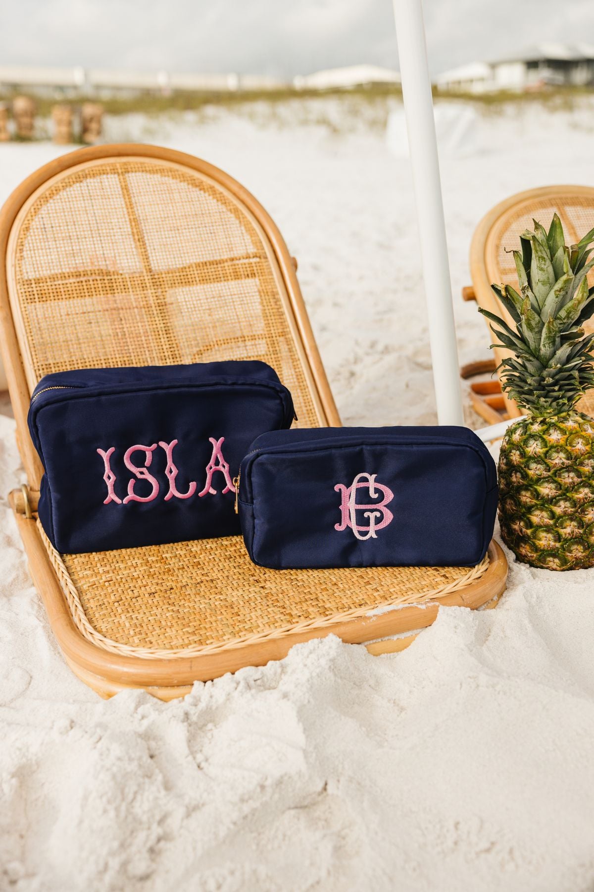 Two navy blue personalized pouches, one larger and the other smaller with both embroidered in pink.