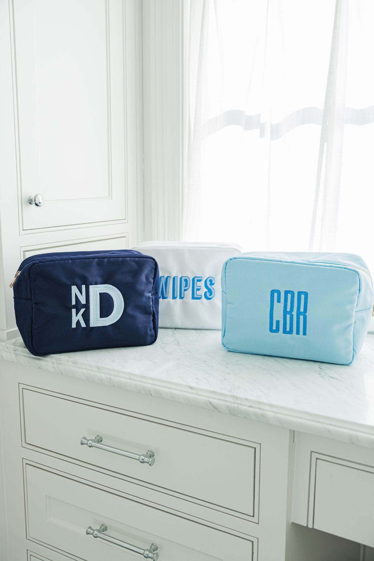  Three rectangular toiletry bags in navy blue, white, and light blue