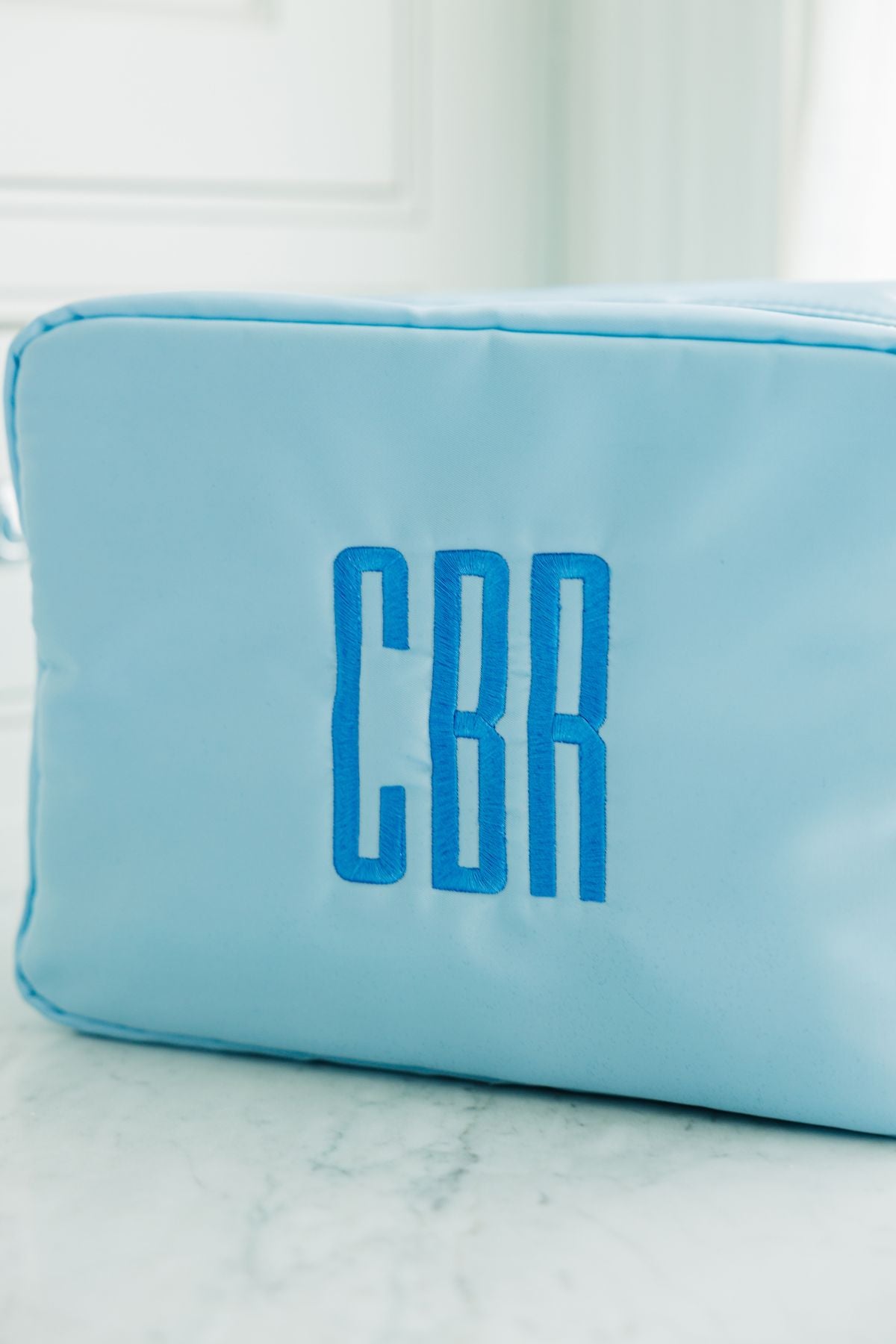 Close-up of a light blue personalized pouch with the initials 'CBR' embroidered