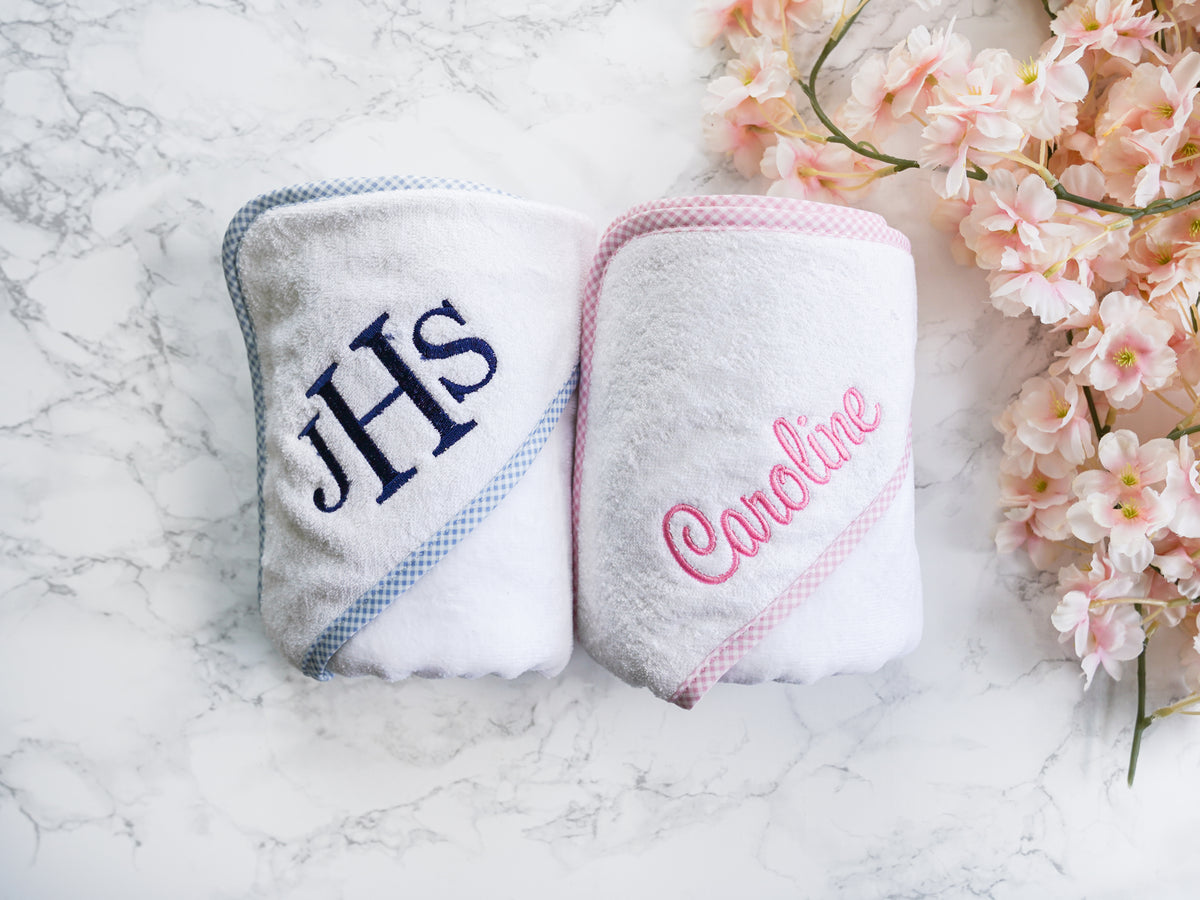 Two white hooded towels, one with blue gingham trim and the other with pink gingham.