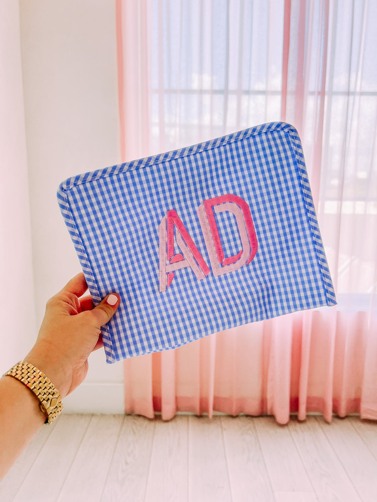 Blue gingham pouch with 'AD' monogram embroidered in pink.