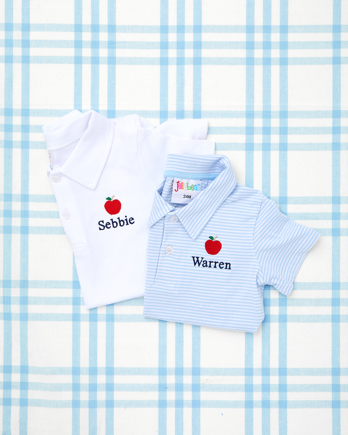 Two Solid Short Sleeve Polos with Motif, featuring embroidered red apple designs and personalized names—one in crisp white with “Sebbie” and the other in soft blue and white stripes with “Warren.” These classic collared polos are perfect for a polished and playful back-to-school look.