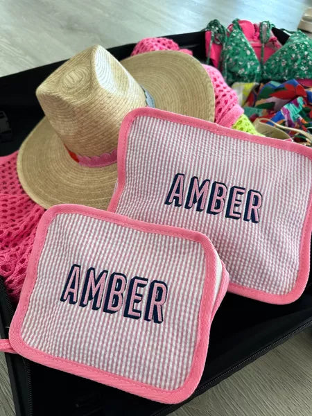 Two pink-striped pouches with 'Amber' monogrammed in bold navy blue lettering, each outlined with pink trim.