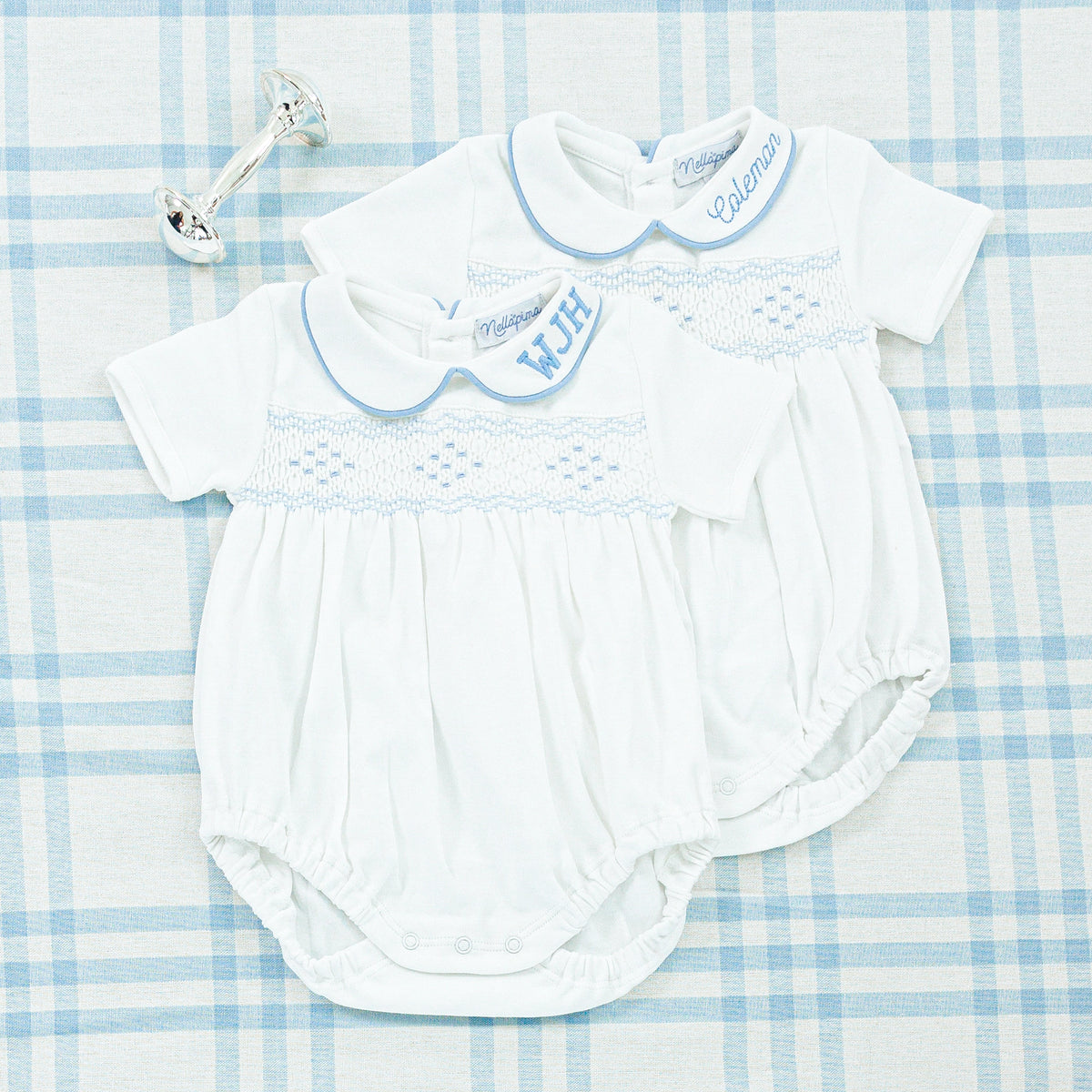A close-up of two white baby onesies with light blue smocking and personalized monograms 