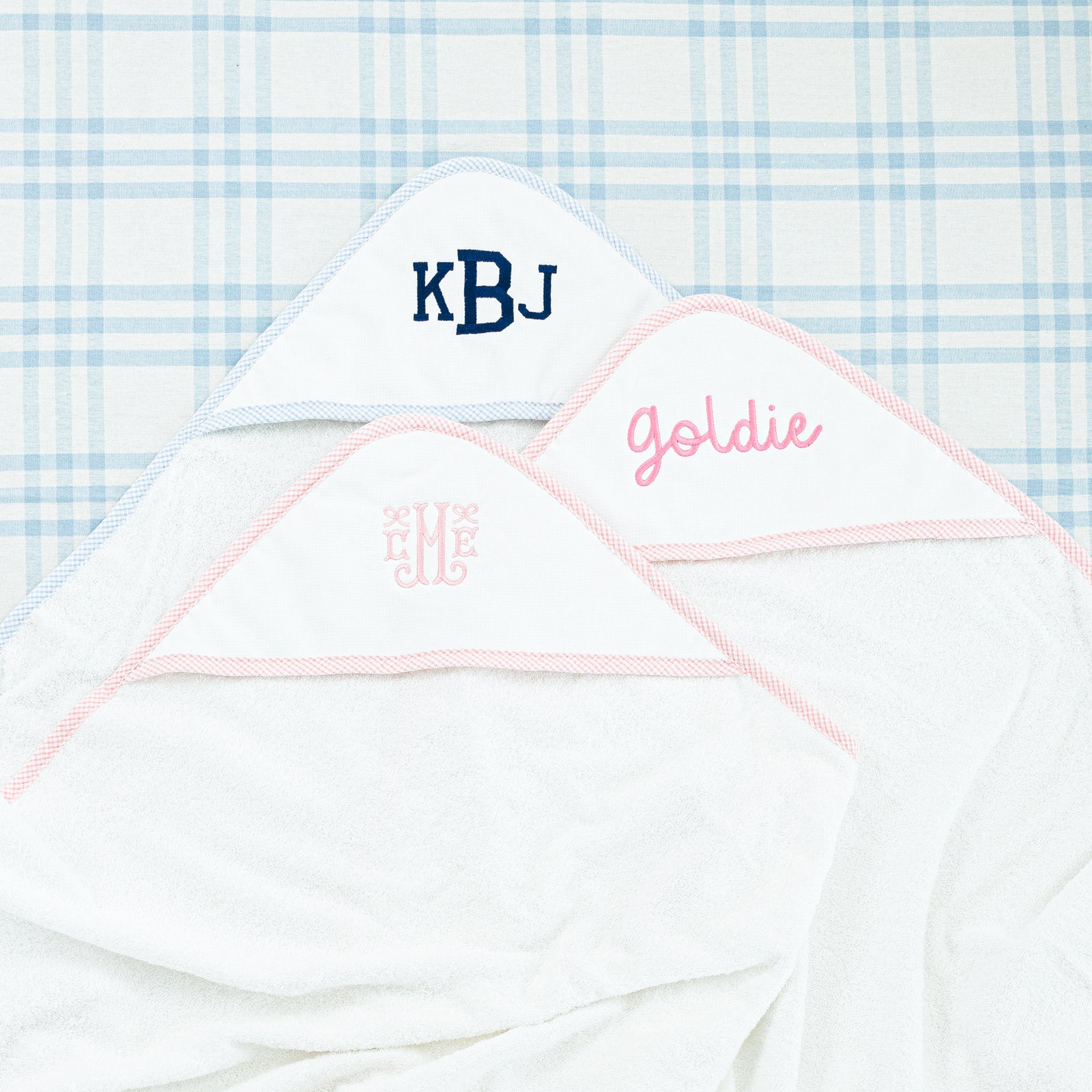 Two white hooded towels: a light blue gingham trim with 'KBD' and a pink gingham trim.