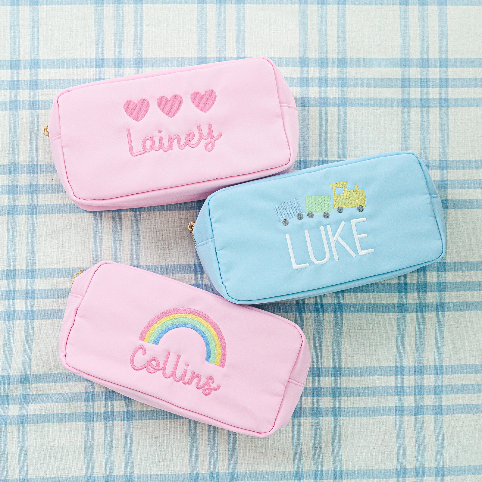 Three colorful pouches displayed: one in blue, one in white, and one in pink with motif.
