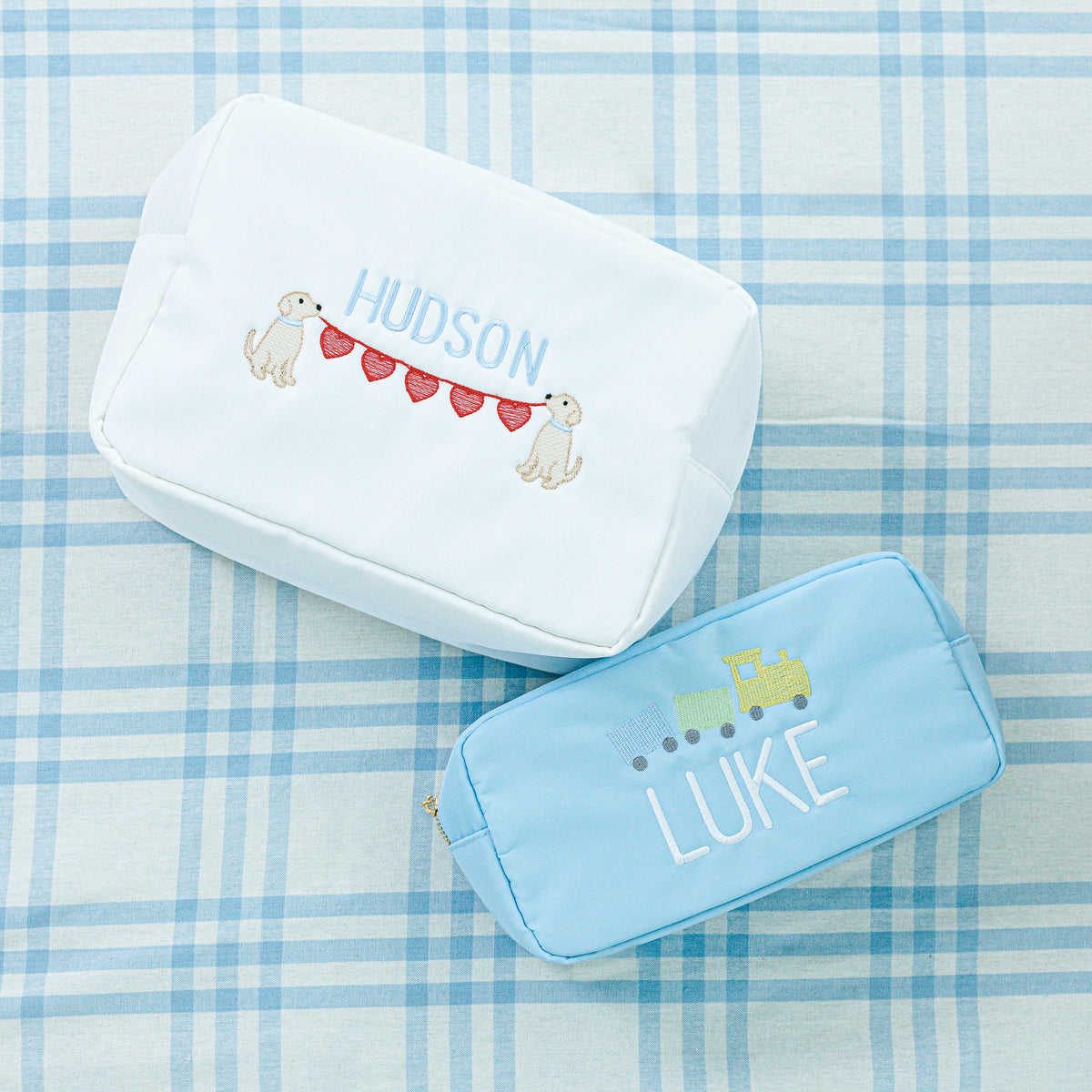 Two personalized pouches. The top pouch is white with 'Hudson' embroidered in blue