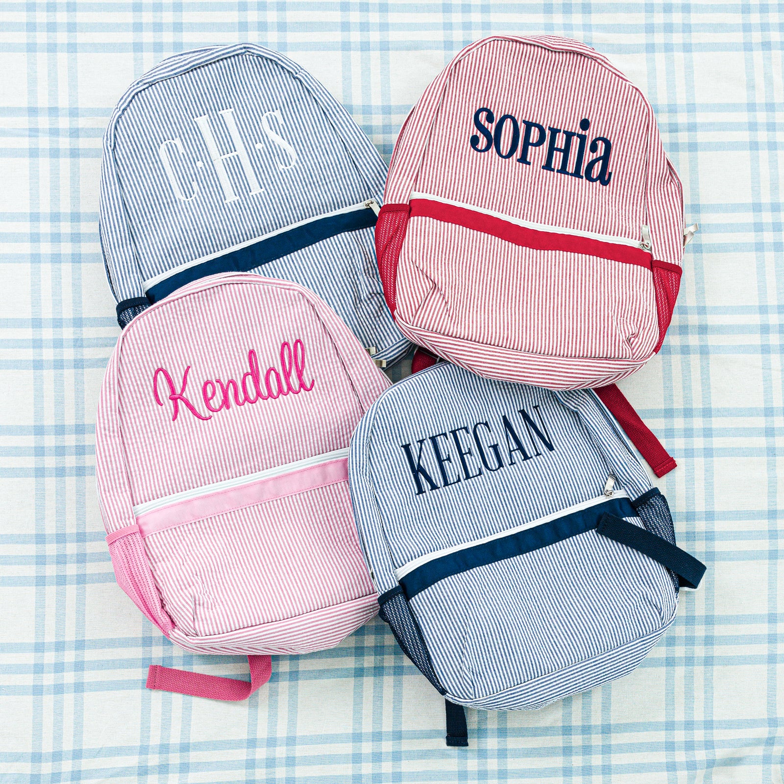 Two personalized seersucker backpacks: a pink backpack with 'CHB' initials and a blue backpack with 'Mason' name.
