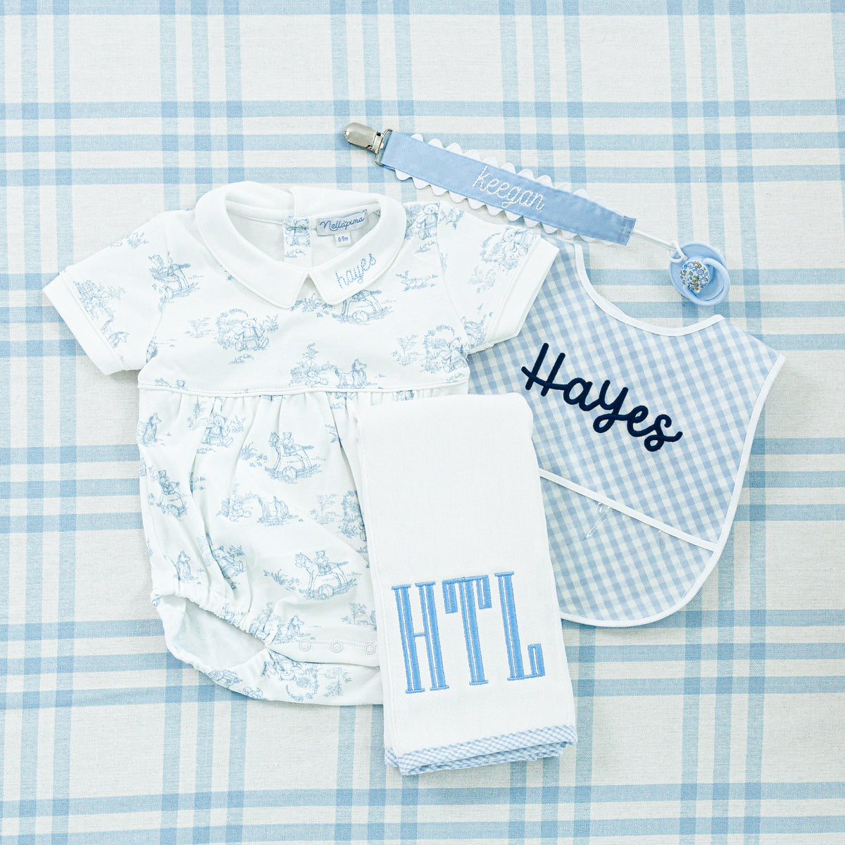 A coordinated baby gift set featuring a blue toile onesie with 'Hayes' embroidered on the collar