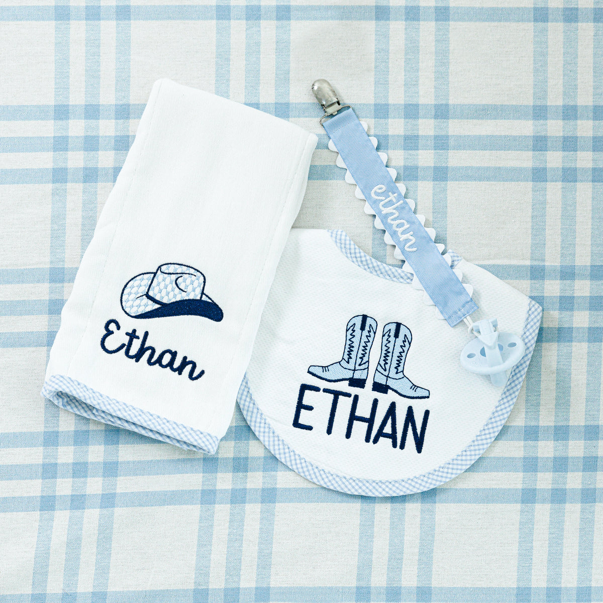 A personalized baby gift set featuring a white washcloth with a cowboy hat and 'Ethan' embroidered in navy blue