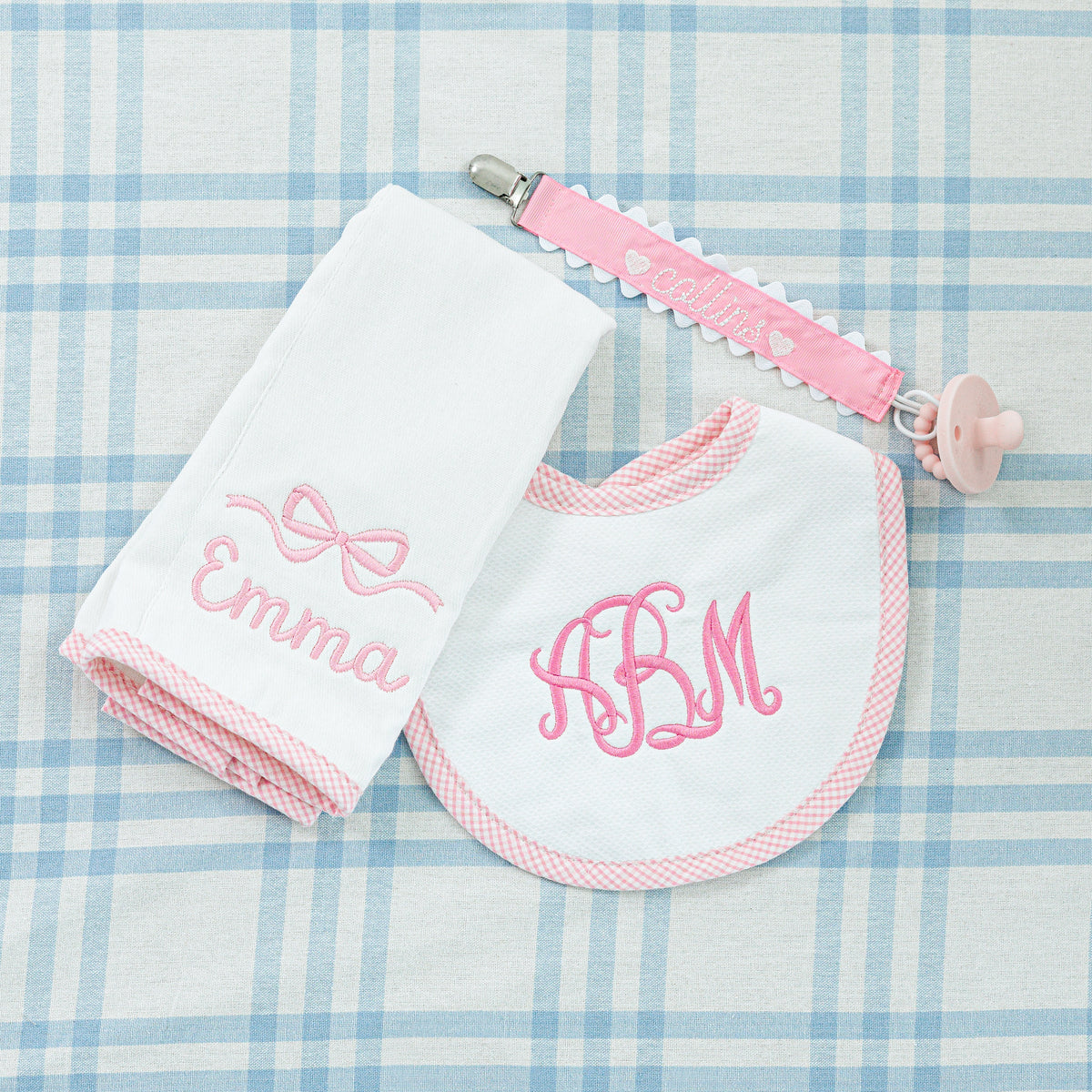 Personalized baby gift set featuring a pink pacifier clip, a bib and a towel.