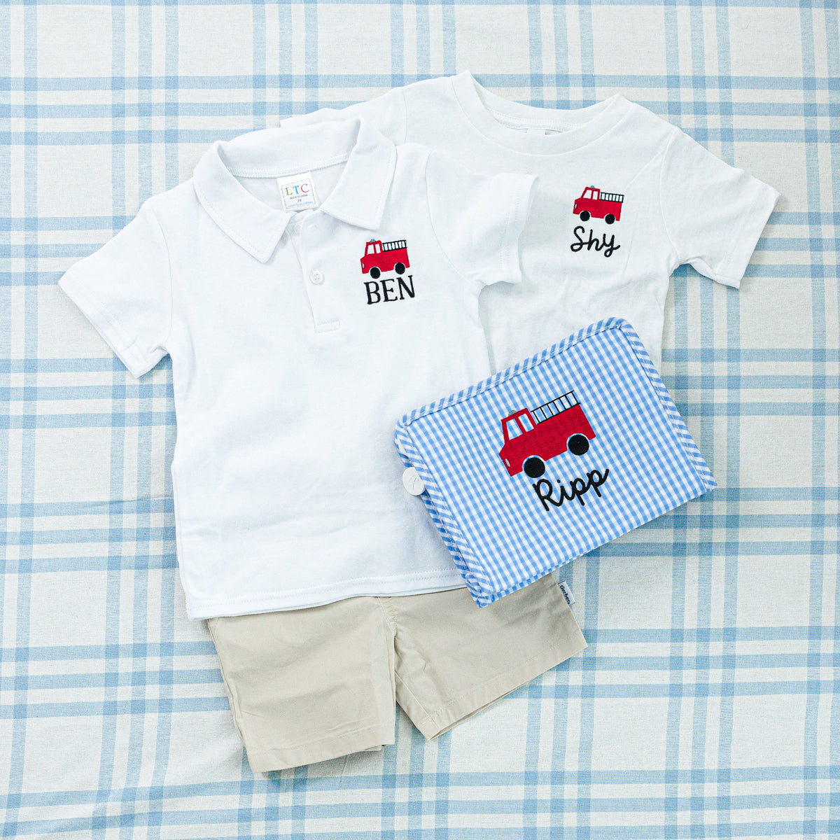 Children's outfit set featuring a white polo shirt, t-shirt and a blue gingham pouch embroidered with a fire truck.
