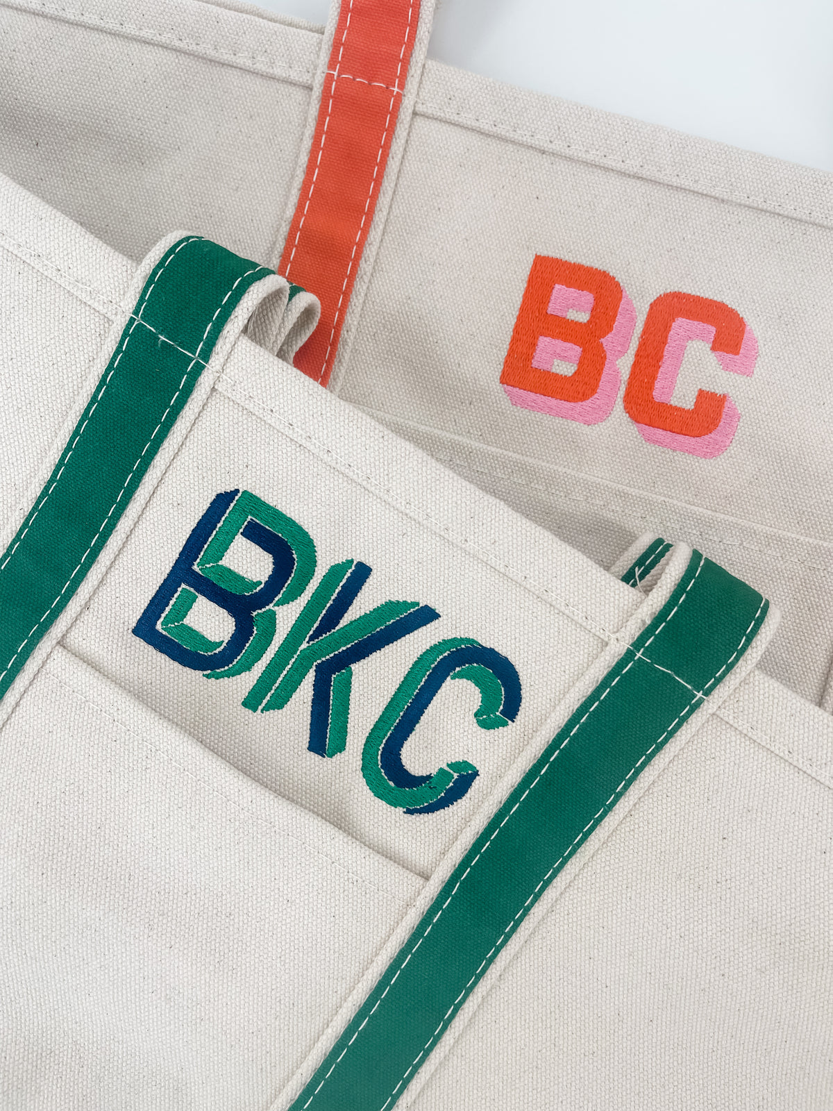 Close-up of two canvas tote bags with green and orange handles