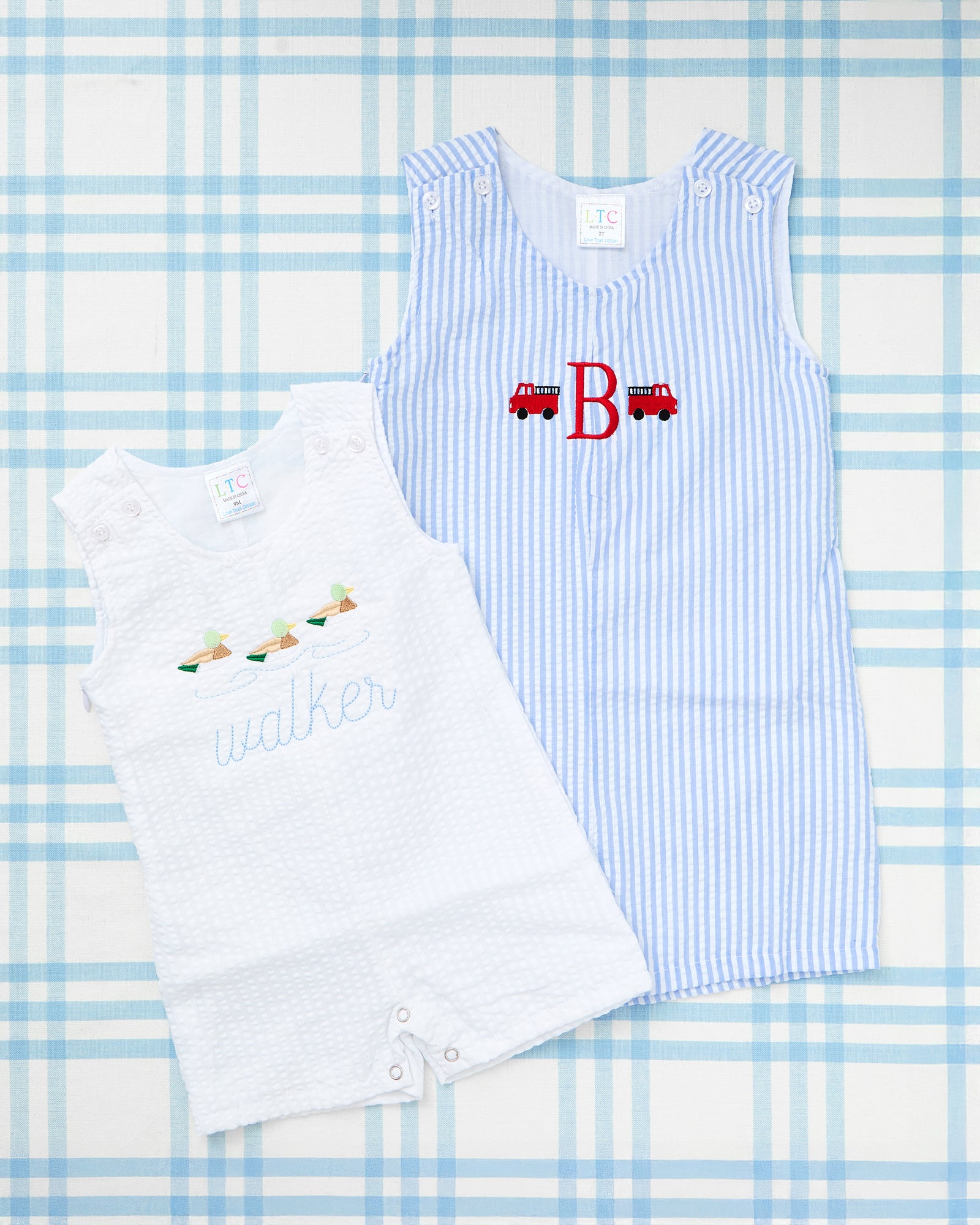 Image featuring two personalized baby outfits. On the left is a Seersucker Jon Jon with Motif, showcasing light blue and white stripes, embroidered fishing lures, and the name “whitman” in navy script. On the right is a crisp white jon jon featuring a sporty embroidered crest with a red "C" monogram flanked by crossed bats, adding a classic and playful touch. Both pieces are ideal for summer-ready, monogrammed toddler styles.