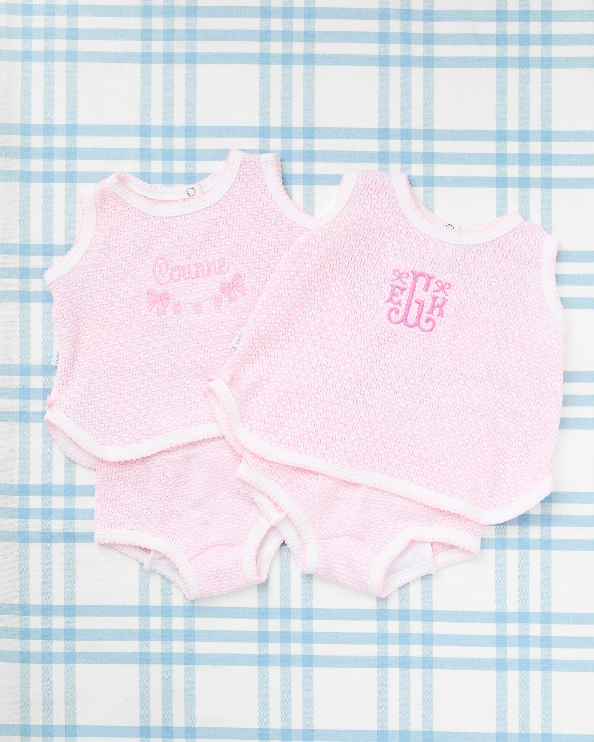 Sleeveless Knit Diaper Cover Set with Motif from Rainey Laine featuring two soft pink textured sets—one with the name "Corinne" and bow-and-heart embroidery, and the other with an elegant monogram "ELH"—styled on a blue plaid background for a sweet, classic baby look.