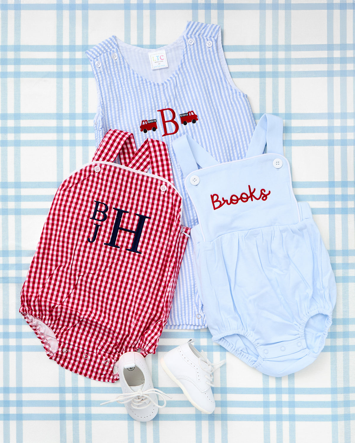 Seersucker Jon Jon with Motif featuring a firetruck and monogrammed "B" design in light blue, paired with a red Gingham Sunsuit with Motif monogrammed "BJH" in navy—classic Southern-inspired outfits for little boys, styled with white leather baby shoes.