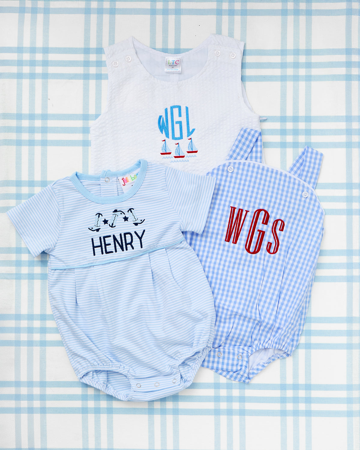 Seersucker Jon Jon with Motif featuring monogrammed initials "WGL" and sailboat embroidery, styled alongside a classic blue Gingham Sunsuit with bold red "WGS" monogram and a coordinating striped Short Sleeve Bubble with dancing boot motif and the name "Henry."