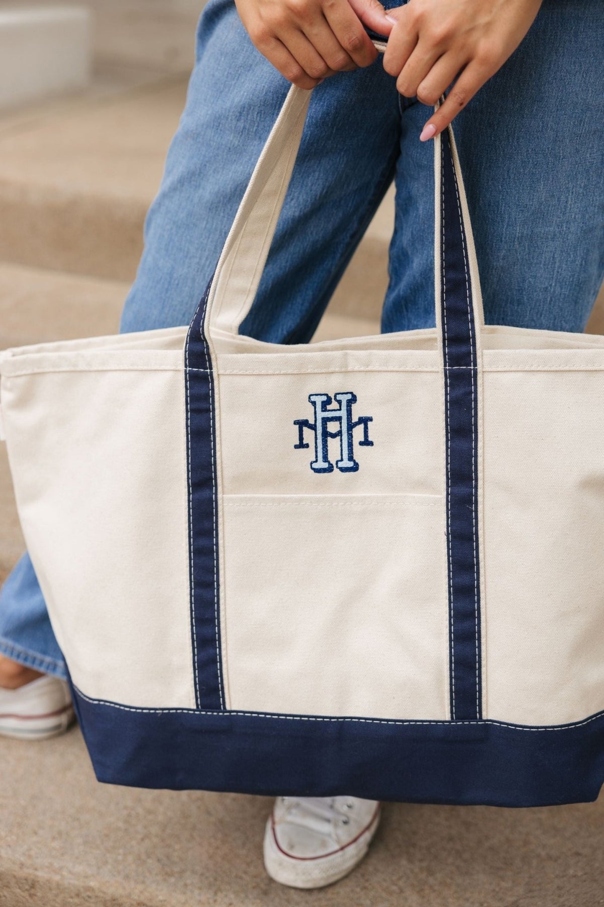 Canvas tote bag with navy blue handles and a matching navy blue bottom. The tote features a front pocket.