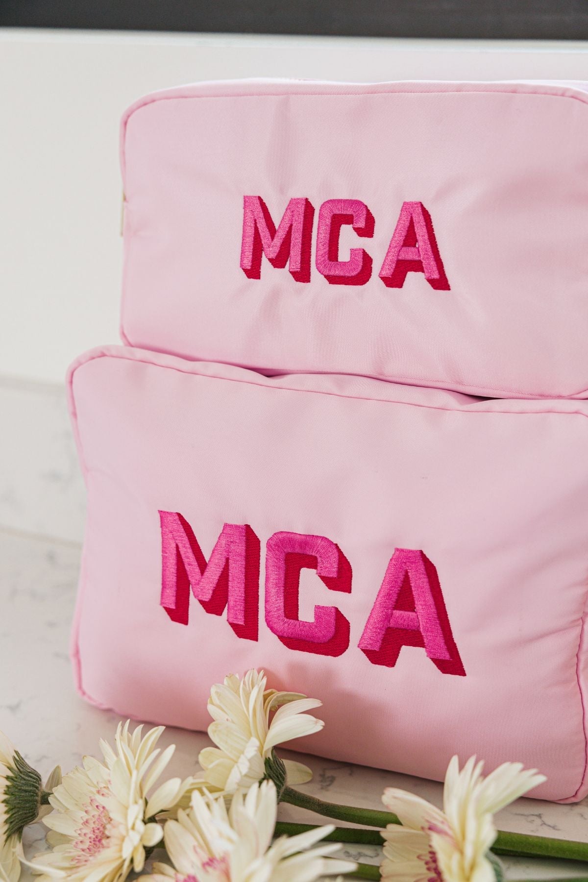  Two pink rectangular toiletry bags in different sizes with embroidered initials.