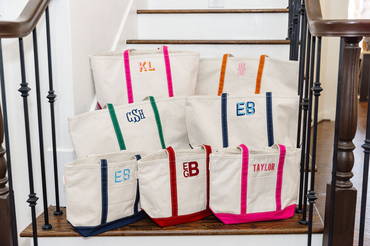 A collection of canvas tote bags in various sizes, each featuring different colored handles