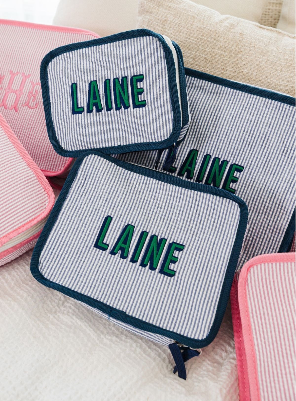 Seersucker fabric pouches with navy trim, each embroidered with the name 'Laine' 