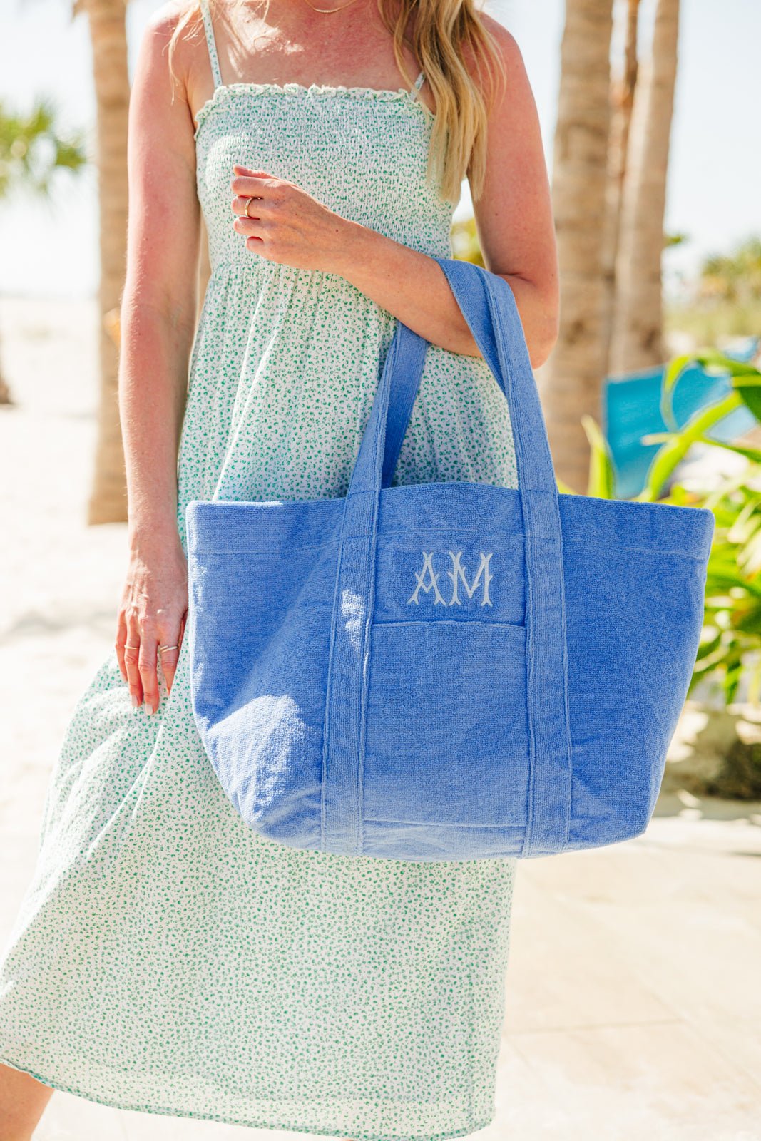 Woman holding a spacious embroidered terry tote in soft blue, featuring custom monogram initials stitched on the front pocket. This plush, towel-textured bag blends comfort and functionality—perfect for beach days, poolside lounging, or summer errands in style.