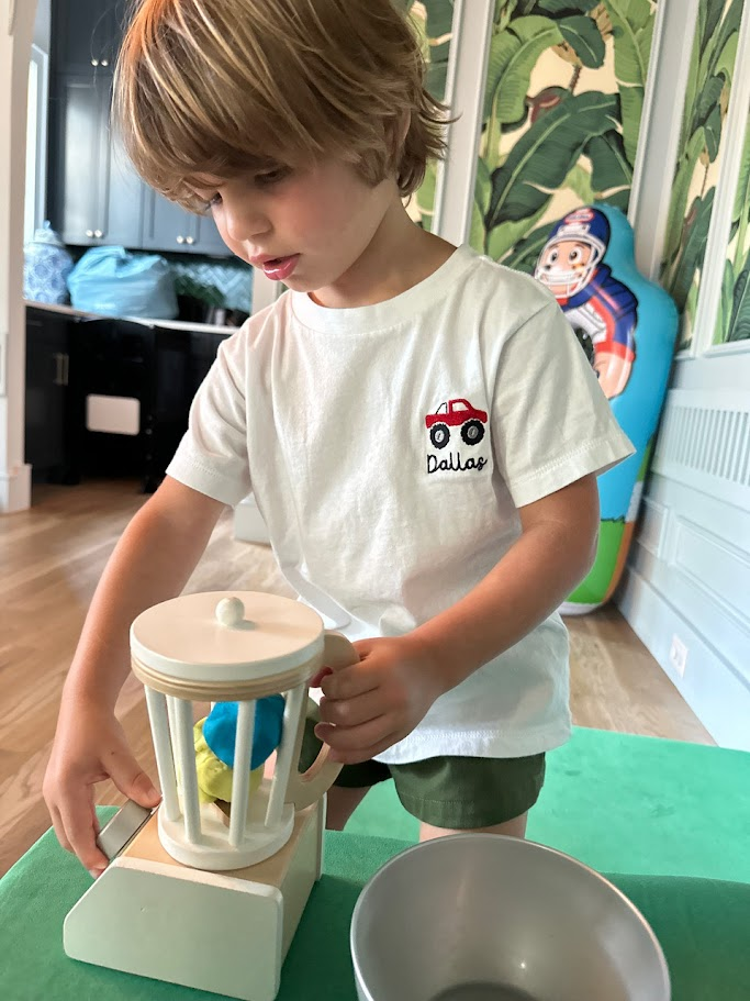 Child wearing a white t-shirt with an embroidered red toy truck